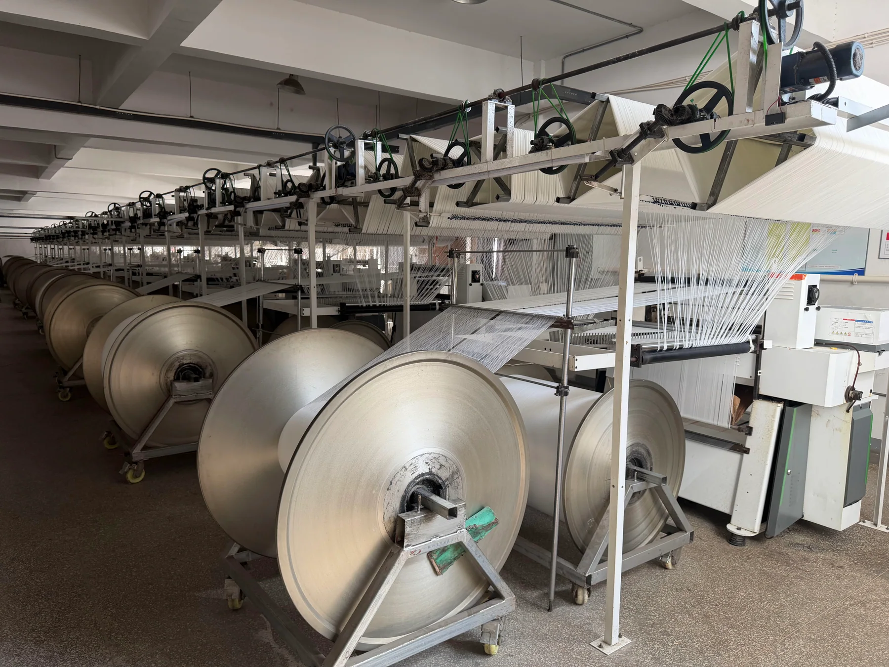 Multiple textile machines and yarn beams arranged across the weaving workshop